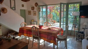A dining area with a table set for four, surrounded by chairs. There is a staircase to the left, a window with a view of trees, and a television on a stand to the right. - Eco-friendly house in a quiet location, one hour from the ocean  (Salernes)