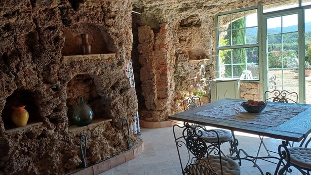 A rustic stone interior with a table and chairs, a window with a view, and shelves with pottery. - Eco-friendly house in a quiet location, one hour from the ocean  (Salernes)