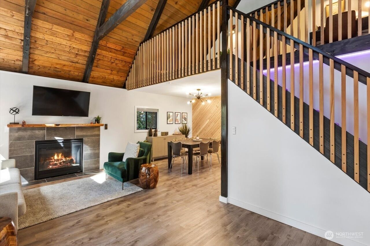 A spacious living room with a fireplace, a dining area, and a staircase with wooden railings.