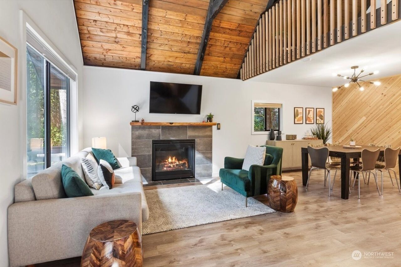 A modern living room with a fireplace, a television mounted above it, and a dining area with a wooden ceiling.