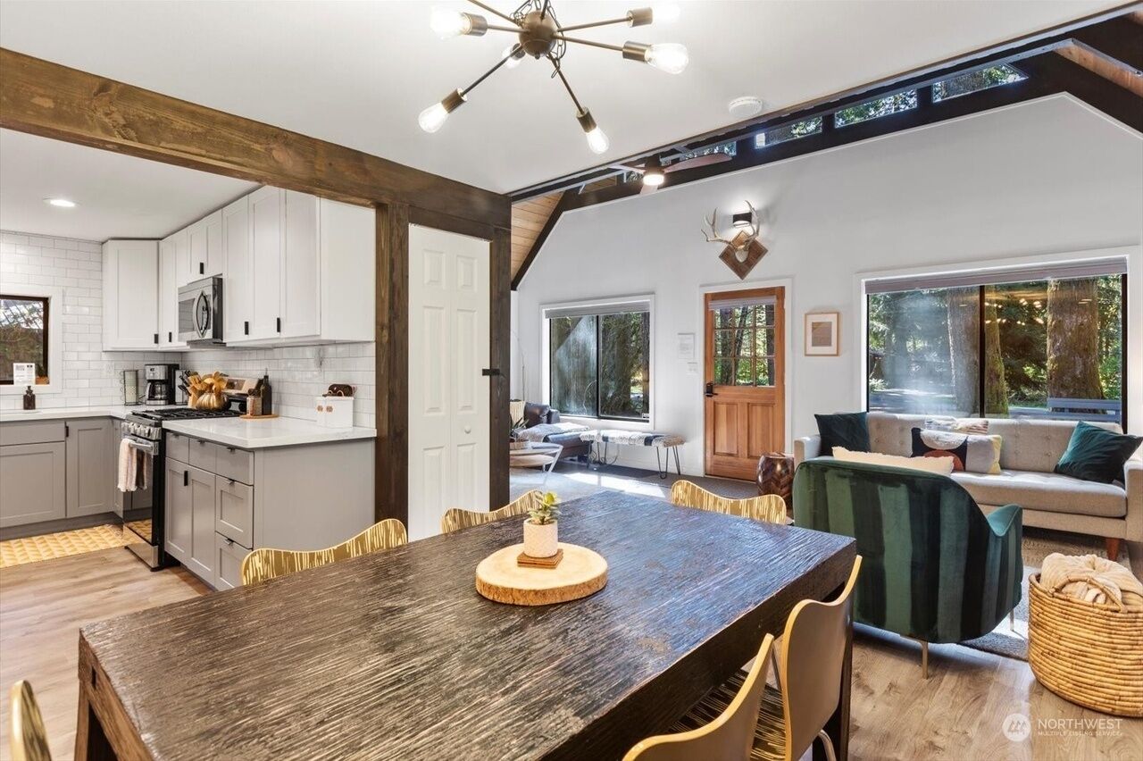 A modern kitchen with white cabinets, a wooden dining table, and a chandelier.