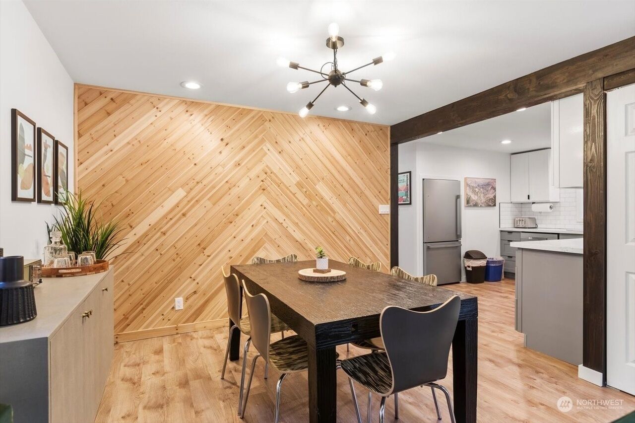 A modern kitchen with white cabinets, a central island, and a herringbone wood wall.