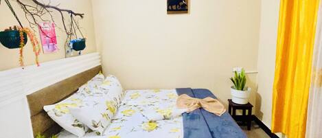 A bedroom with a bed, a bedside table, a small potted plant, a wall-mounted air conditioner, and a yellow curtain.
