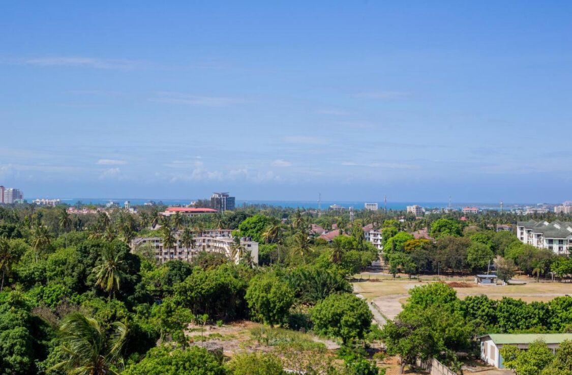 A coastal cityscape with dense greenery, buildings, and a clear view of the ocean.