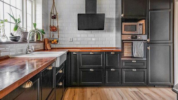 Una cocina moderna con armarios oscuros, encimera de madera, un colgador para ollas y un microondas y horno integrados.