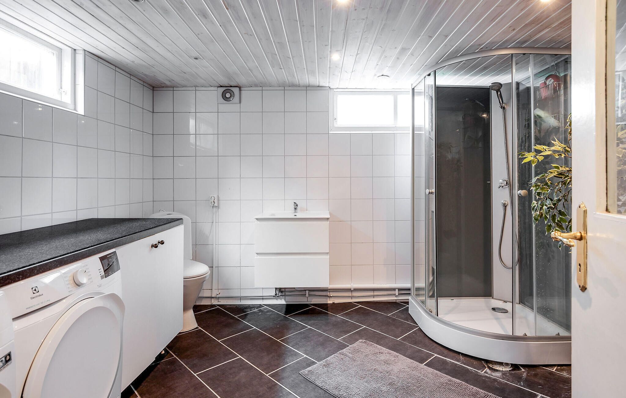 A modern bathroom with a washing machine, toilet, and a glass-enclosed shower.