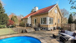 Una casa con piscina, terraza de madera y mobiliario exterior.
