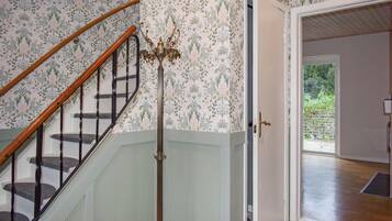 A staircase with a wooden handrail and black balusters, leading to a room with floral wallpaper and a door leading outside.
