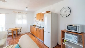 A compact kitchen with a dining area, a clock, and a microwave on a shelf.
