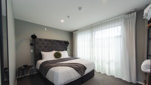 Ein modernes Hotelzimmer mit einem großen Bett, einem Kopfteil, einem Nachttisch und einem Fenster mit Vorhängen.