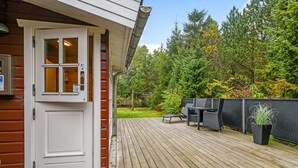 Una terraza de madera con mobiliario exterior y una puerta que da a una habitación.