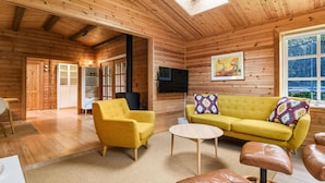 Acogedor interior de cabaña de madera con sofá, sillón y televisor.