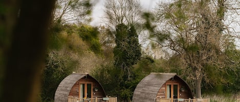 Two wooden dome-shaped cabins with wooden decks and picnic tables, surrounded by trees and grass.
