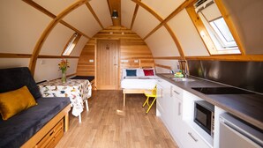 Una habitación compacta y bien iluminada con una cama, un sofá, una mesa de comedor y una kitchenette.