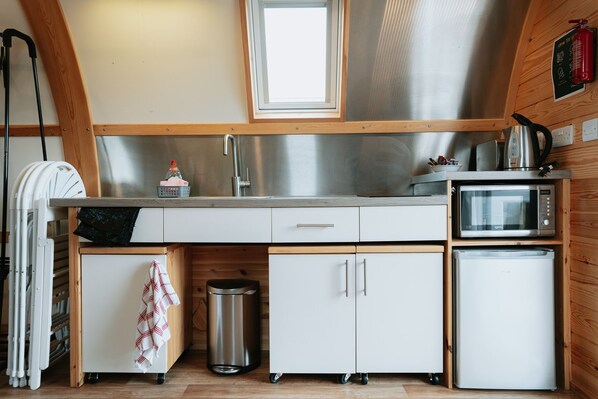 Una cocina compacta con un lavamanos de acero inoxidable, un microondas y un refrigerador pequeño.