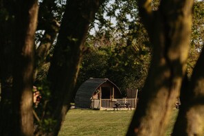 Une petite structure rustique en bois, dotée d’un toit en pente, entourée d’une terrasse en bois et d’une zone herbeuse.