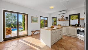 Una cocina moderna con una isla central, armarios blancos y vistas a una piscina a través de amplios ventanales correderas.