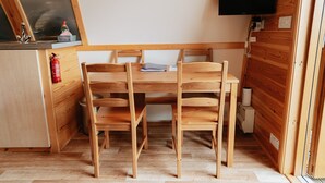 Une pièce en bois de taille réduite, comprenant une table et des chaises, un petit coin cuisine et un téléviseur fixé au mur.