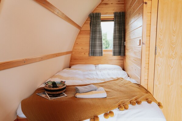 Ein gemütliches Schlafzimmer mit Holzbalkendecke, einem Bett mit weißer Bettwäsche, einer braunen Tagesdecke und einem kleinen Tisch mit einem Korb und einer Zeitschrift.