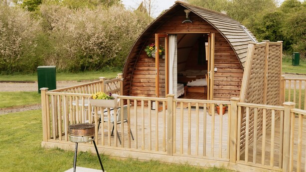 Une cabane en bois avec un balcon, un barbecue et une petite table avec des chaises.