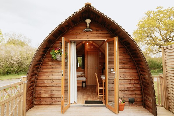 Une cabane en bois avec une porte ouverte, un lit, une chaise et une petite table à l’intérieur.