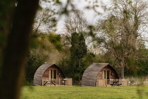 Deux cabanes en bois en forme de dôme, dotées de terrasses en bois et de tables de pique-nique, entourées d’arbres et d’herbe.