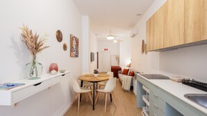 Eine moderne Küche mit Holzausstattung, ein Essbereich mit rundem Tisch und Stühlen sowie eine kleine Wohnzone mit Sofa und Fernseher.