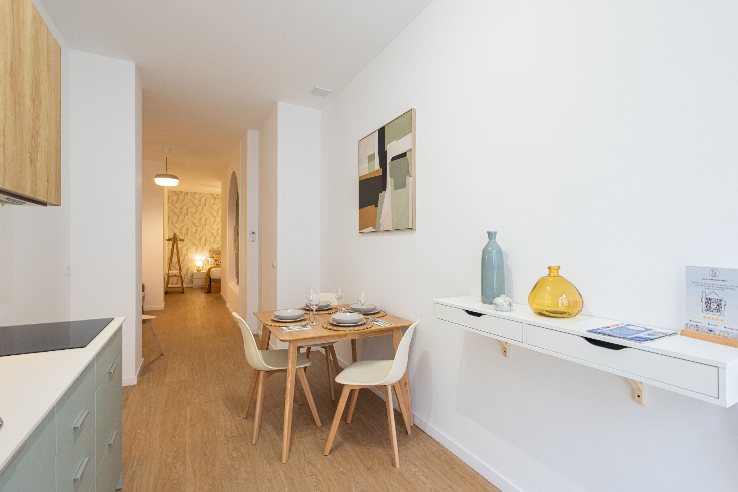 Un espace repas moderne avec une table et des chaises en bois, un comptoir blanc et une étagère ornée d’objets décoratifs.