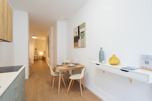Ein zeitgemäßer Essbereich mit einem Holztisch, Stühlen, einer weißen Arbeitsplatte und einem Regal mit Dekoration.