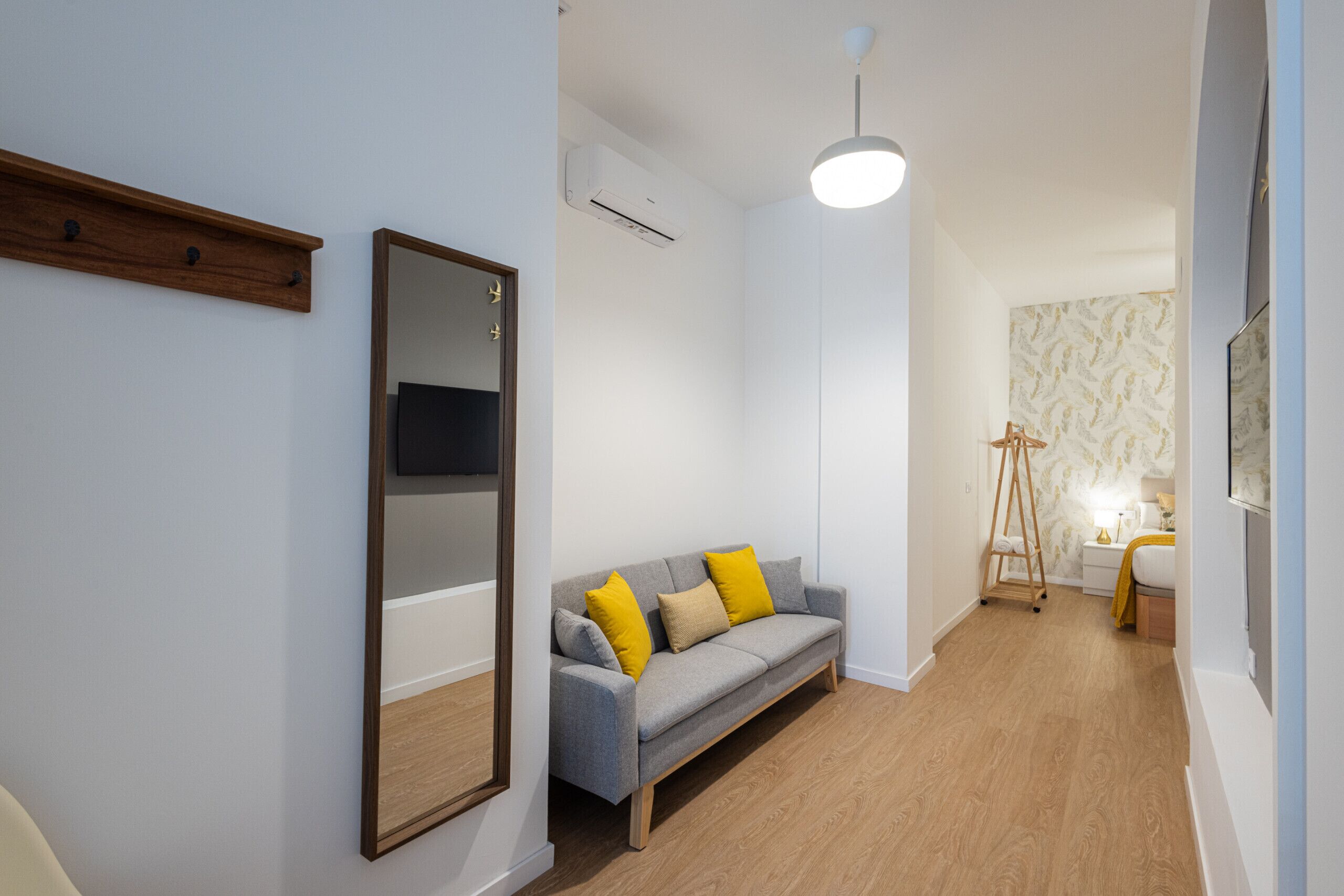 A modern living room with a grey sofa, wooden floor, and a large mirror.