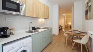 A compact kitchen with a microwave, coffee maker, and washing machine. There is a dining area with a table set for four.