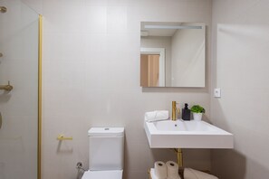 Ein Badezimmer mit Toilette, Waschbecken mit Spiegel und Duschbereich.