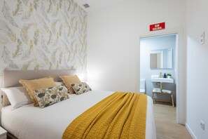 Ein Schlafzimmer mit Bett, Kissen, einer gelben Decke, einem Badezimmer mit Waschbecken und Spiegel sowie einem Schild an der Wand.