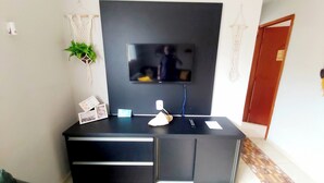 Un saló modern amb un televisor de pantalla plana fixat a una paret fosca, un moble de televisió negre amb calaixos, una làmpada de taula petita i una planta en test.