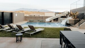 A pool area with a waterfall feature, lounge chairs, and a table. - Sleeps 26! Private Pool, Hot Tub, Theater, & More! (Hurricane)