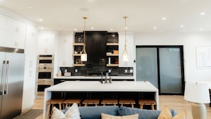 A modern kitchen with white cabinetry, stainless steel appliances, and a central island with bar stools. - Sleeps 26! Private Pool, Hot Tub, Theater, & More! (Hurricane)