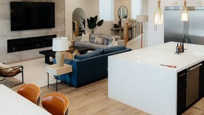A modern living room with a sofa, a TV, and a dining area with chairs and a table. - Sleeps 26! Private Pool, Hot Tub, Theater, & More! (Hurricane)