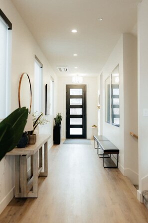 Un couloir avec un banc en bois, une plante en pot et une porte à cadre noir.