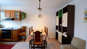 A compact kitchen with wooden cabinets, a dining table with chairs, a built-in bookshelf, and a red rug on the floor. - Apartment With Scenic View (Porec)