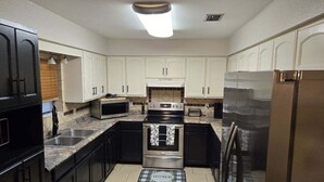 A modern kitchen with dark cabinets, stainless steel appliances, and a tiled backsplash. - Charming 3-bedroom house in lovely McAllen with AC, WiFi, Swimming pool. (McAllen)