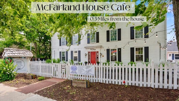 A white house with a red door, a white picket fence, and a sign indicating it is 0.3 miles from the house. - Charming 4 Bed, 2.5 Bath home minutes from Madison perfect for any occasion. (McFarland)