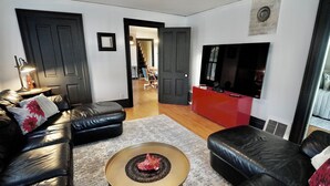 A modern living room with a black leather sofa, a round coffee table, and a flat-screen TV mounted on the wall. - Charming 4 Bed, 2.5 Bath home minutes from Madison perfect for any occasion. (McFarland)