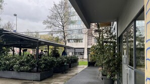 An outdoor seating area with a covered patio, potted plants, and a building with large windows. - Charming Apartment in Nature (Zagreb)