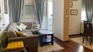 A living room with a sofa, armchair, coffee table, and a dining area with a chair and table. - Charming Apartment in Nature (Zagreb)