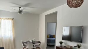 Un saló modern amb un sofà, una taula de menjador preparada per a dues persones, una televisió i un ventilador de sostre.