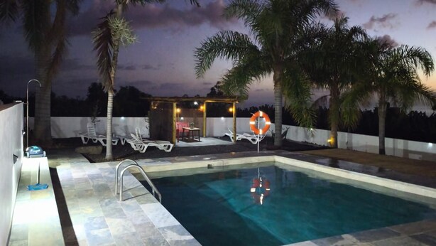 A swimming pool with a tiled deck, surrounded by palm trees and a covered seating area with lights. - Apartment Padres A for 4 People (La Orotava)