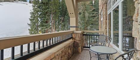 A balcony with stone walls, a wooden railing, and a table with chairs.