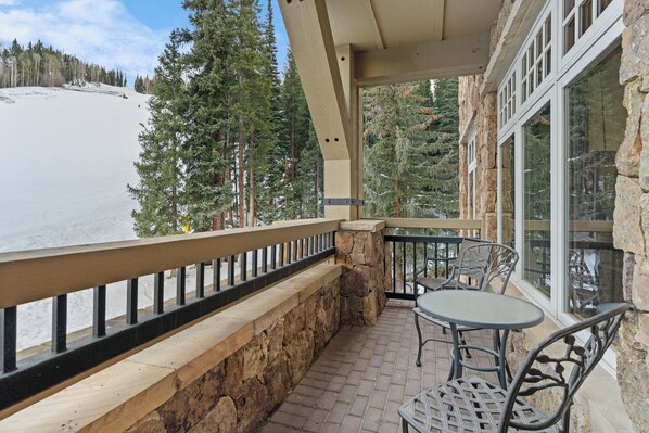 A balcony with stone walls, a wooden railing, and a table with chairs.