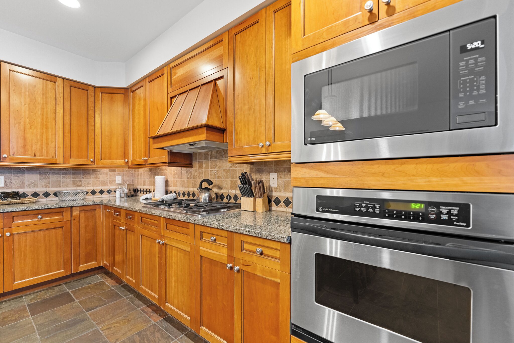 A kitchen with wooden cabinets, a stainless steel microwave, and an oven.