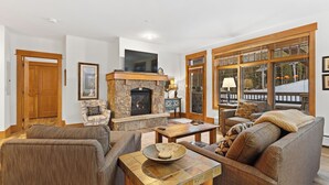 A cozy living room with a stone fireplace, comfortable seating, and large windows offering a view of the outdoors. - Le3012-2 (Keystone)